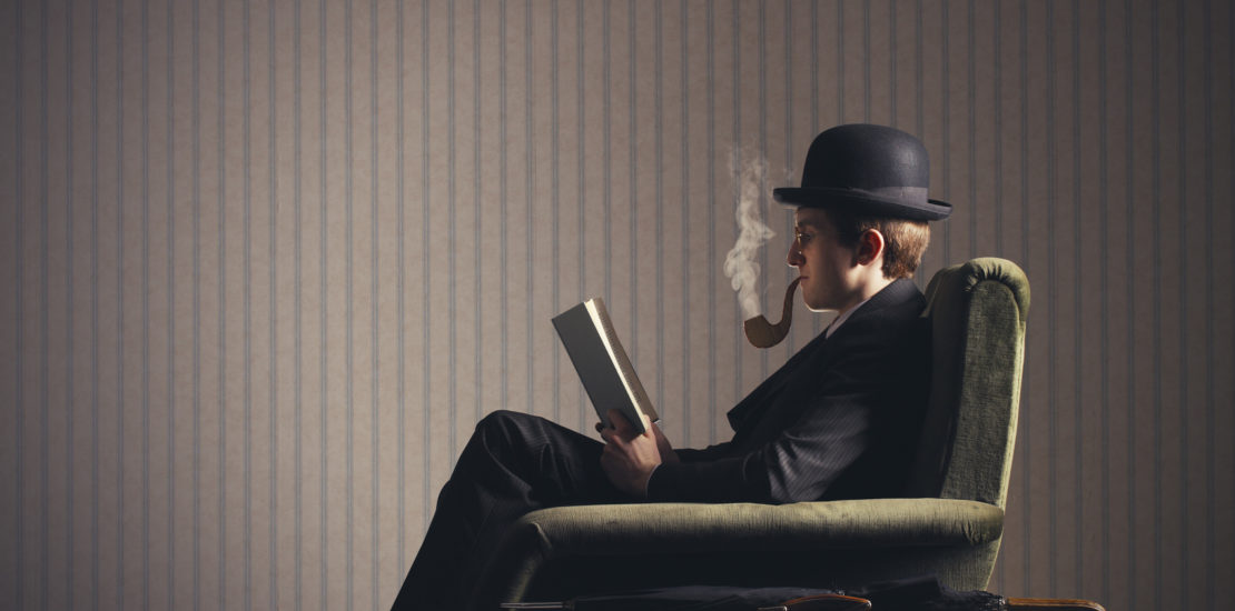 Bizarre man sitting on armchair reading a book and smoking a fake pipe