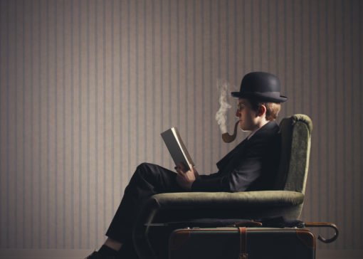 Bizarre man sitting on armchair reading a book and smoking a fake pipe